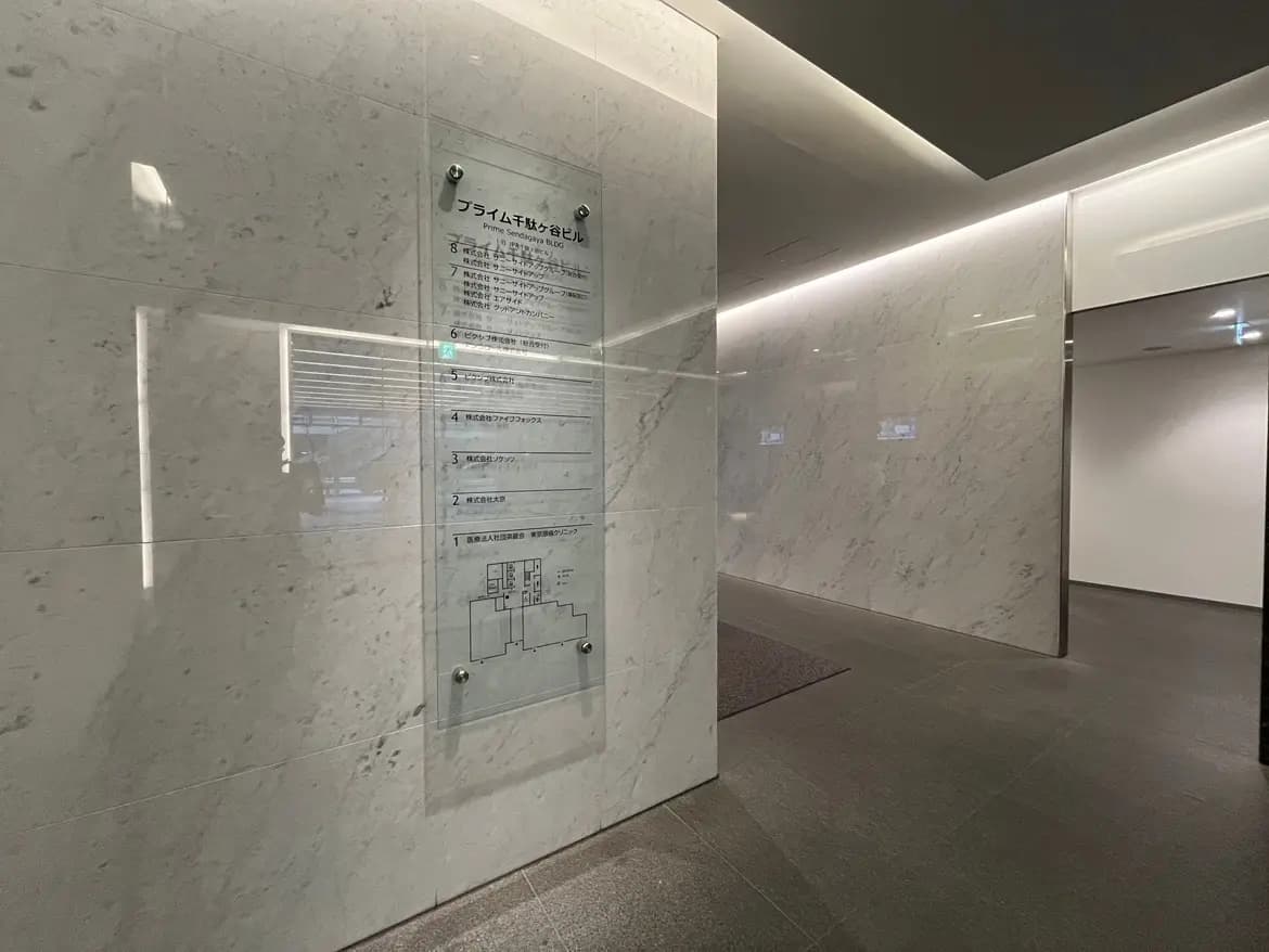 - モダンなオフィスビルのエントランス、グレーの石材壁と案内板、照明が施された明るい空間