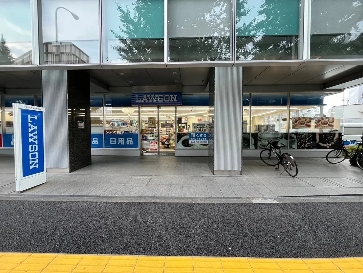 - LAWSONの店舗入口、青い看板とガラス張りの外観、買い物客向けの自転車が停まっている風景