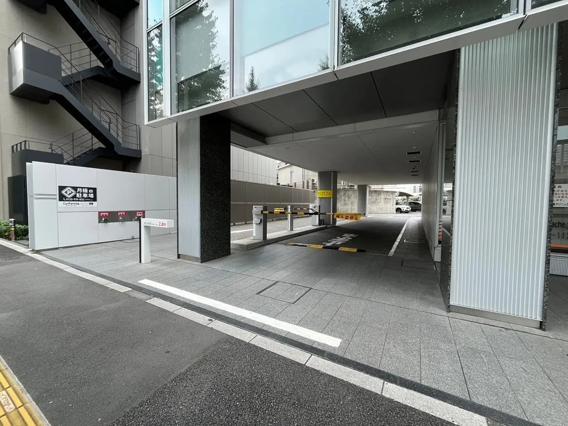 - モダンなデザインの駐車場出入口、スロープと自動ゲートがあり、周囲には植栽と清潔感のある舗装が施されている風景