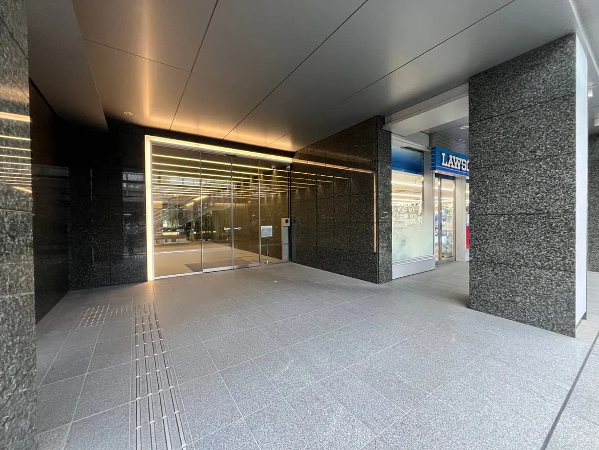 - モダンなエントランスとガラスドア、黒い大理石の壁が特徴的な商業ビルの外観、隣にローソンの店舗がある様子