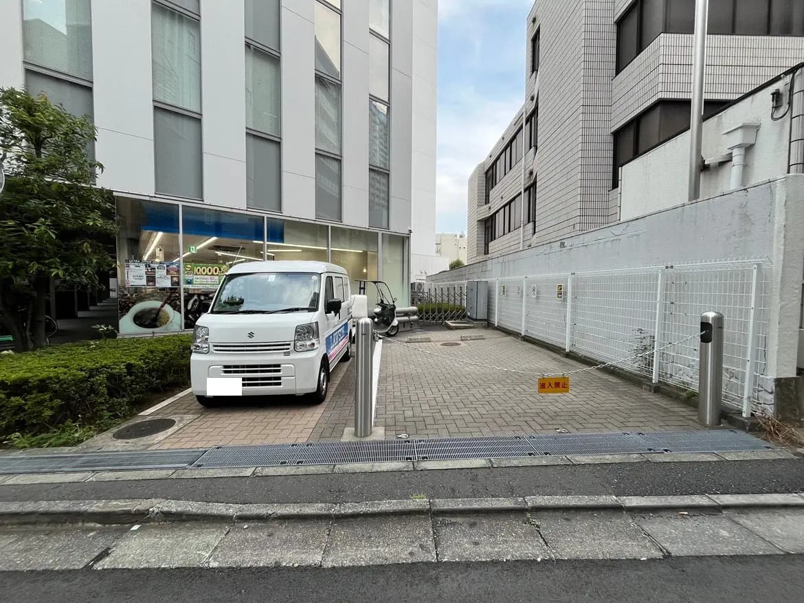 - 駐車場に停まっている白い軽自動車と、周囲にある商業ビルの外観、整然とした舗装された通りの風景