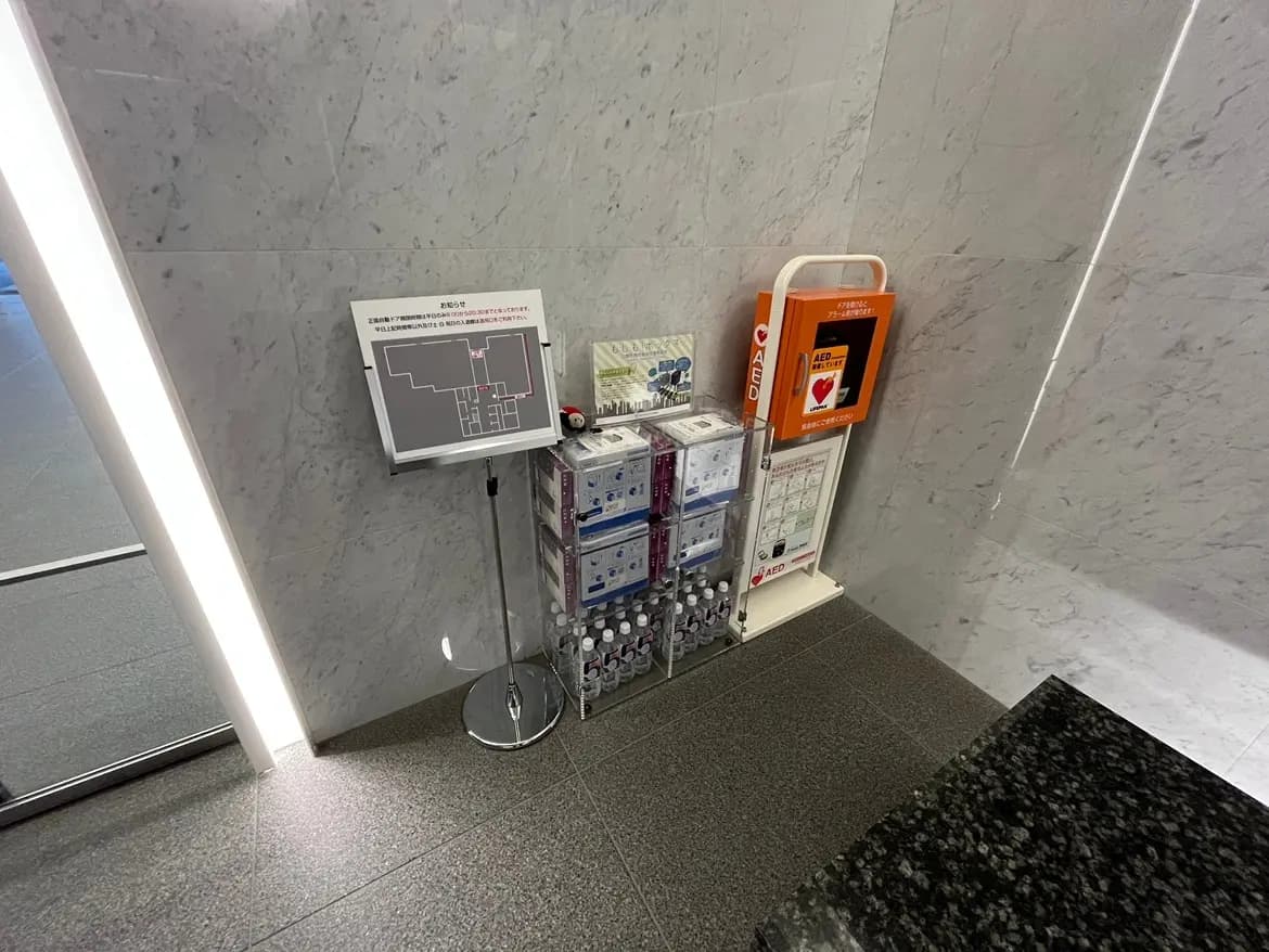 - エントランスの隅に設置された案内板とAED、周囲に設置された自動販売機と水ボトルのディスプレイがある内部の様子