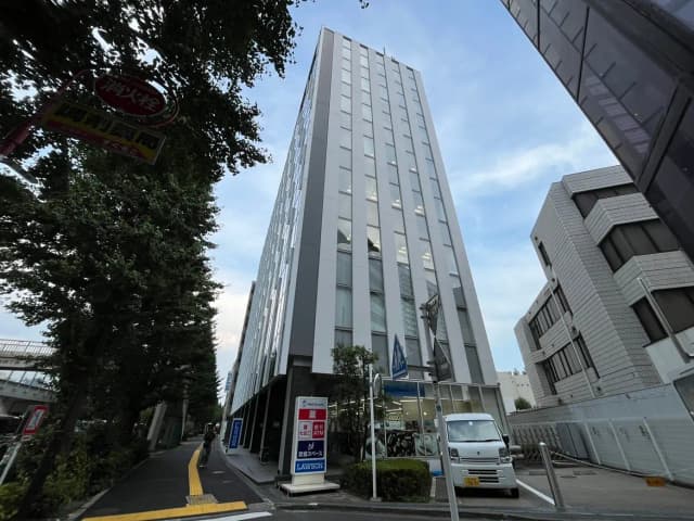 - 近代的なビルが立ち並ぶ街並み、道路沿いに配置された樹木や看板、青空が広がる風景