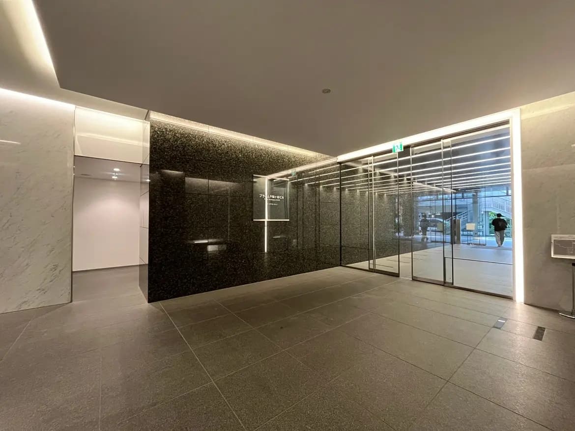 - シックなデザインのロビー、黒い石の壁とガラスドア、明るい間接照明が施されたインテリア