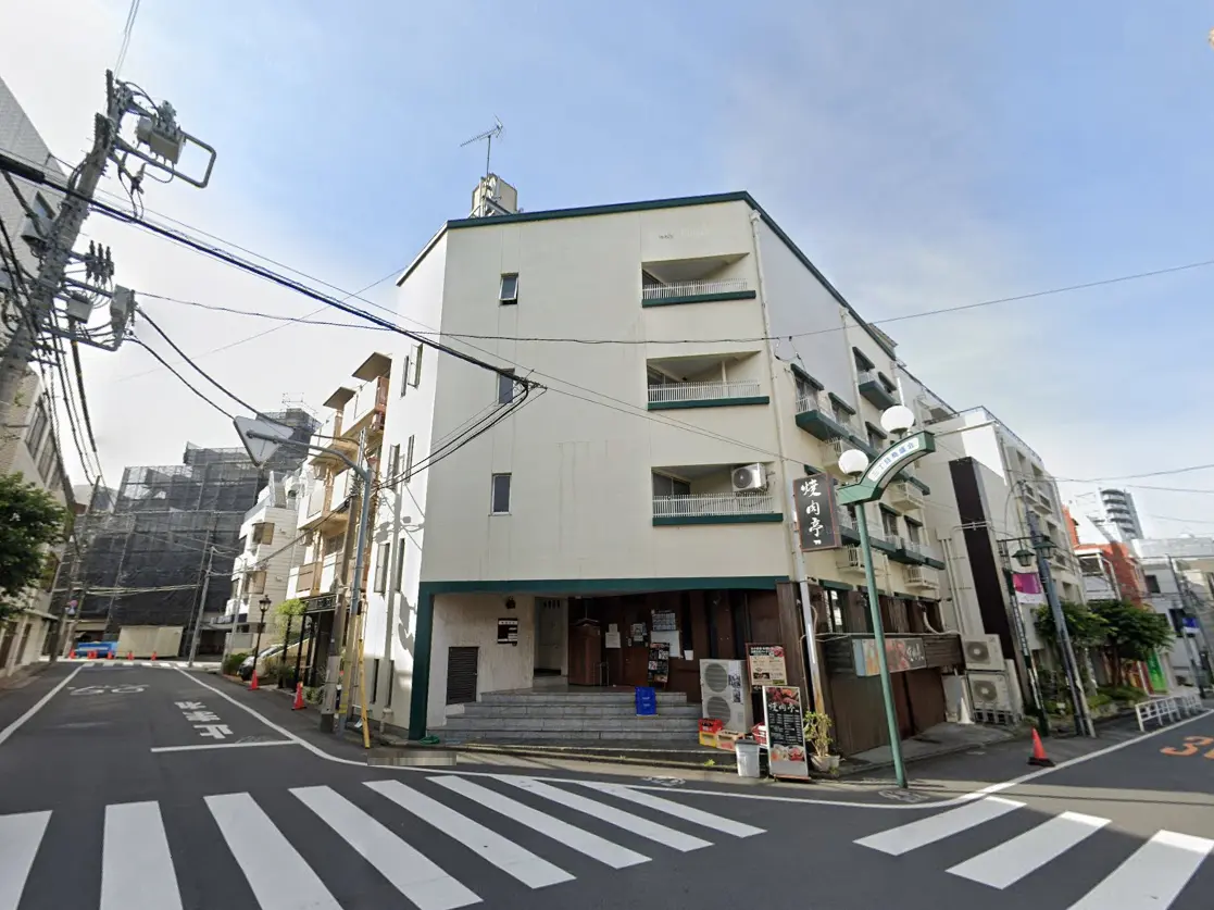 - 街角に位置する外観が白い居酒屋、階段の前に看板が掛かり、周囲に電柱と電線が見える景観