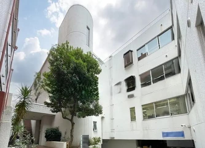 - モダンな建物群に囲まれた、中庭のある白い外壁の建物と緑豊かな樹木の風景