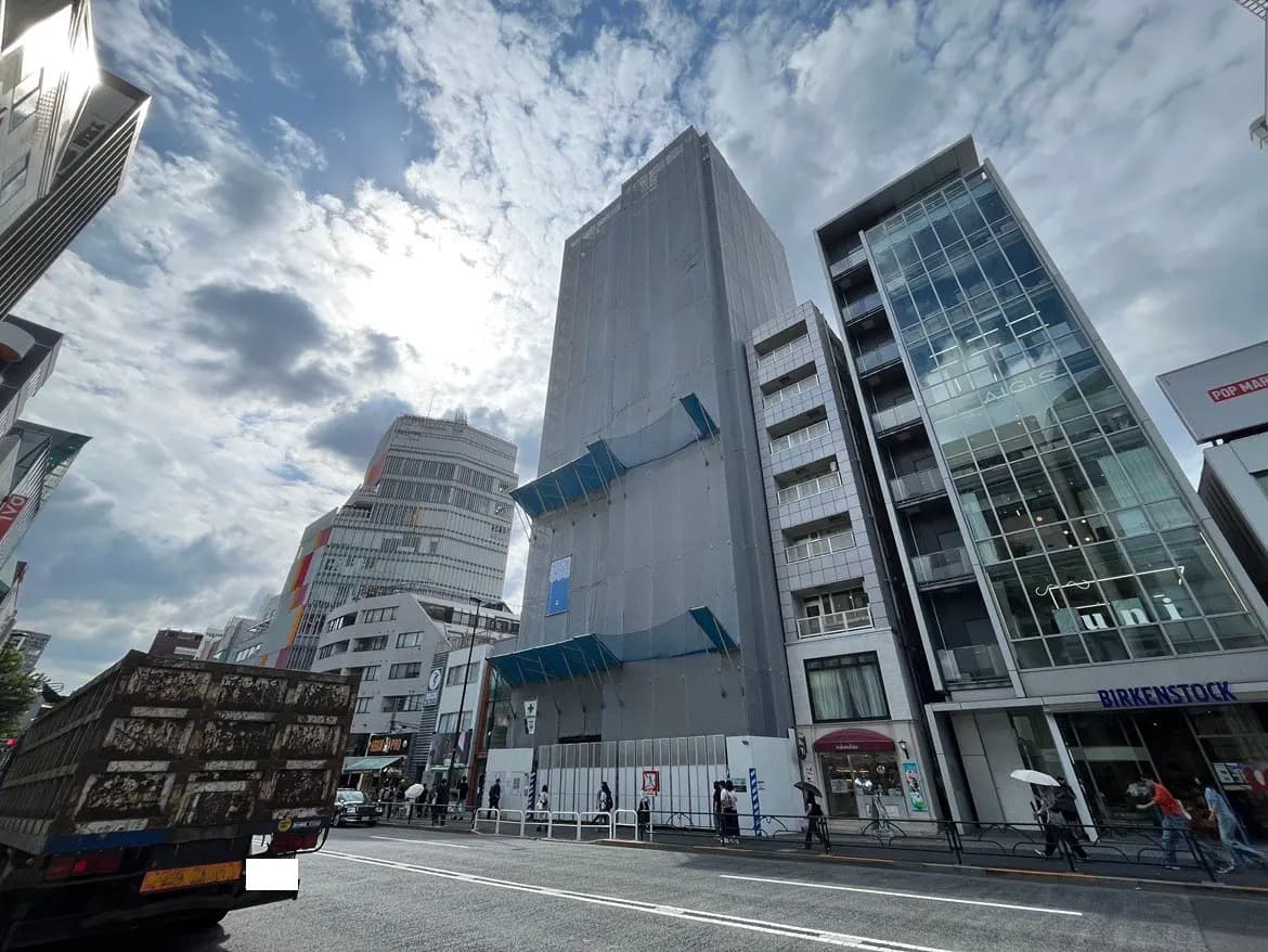 - ビルの建設現場と周囲の商業施設、青空と雲が広がる東京都内の街並みの風景