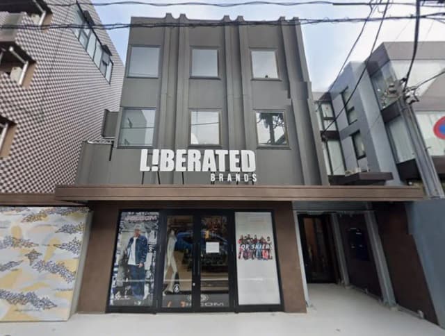 - モダンなデザインの店舗外観、「LIBERATED BRANDS」の看板が掲げられた入り口、隣接する建物とのコントラストが際立つシーン