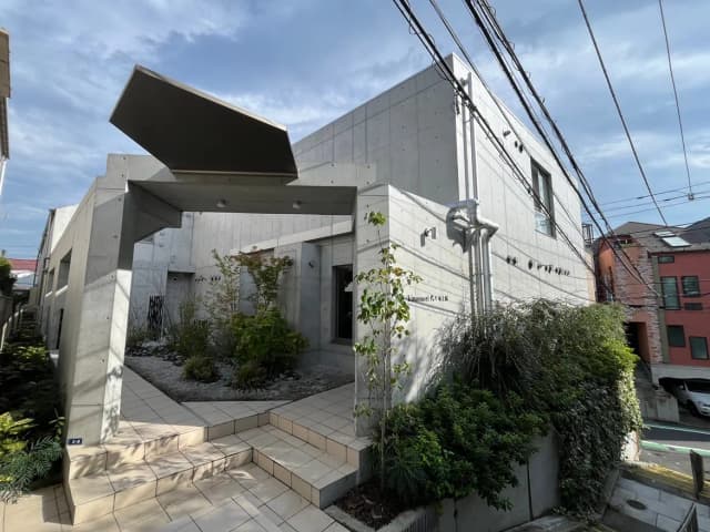 - コンクリート打ちっぱなしの外壁を持つ現代的な住宅、緑豊かな庭と整然としたアプローチが特徴的な外観