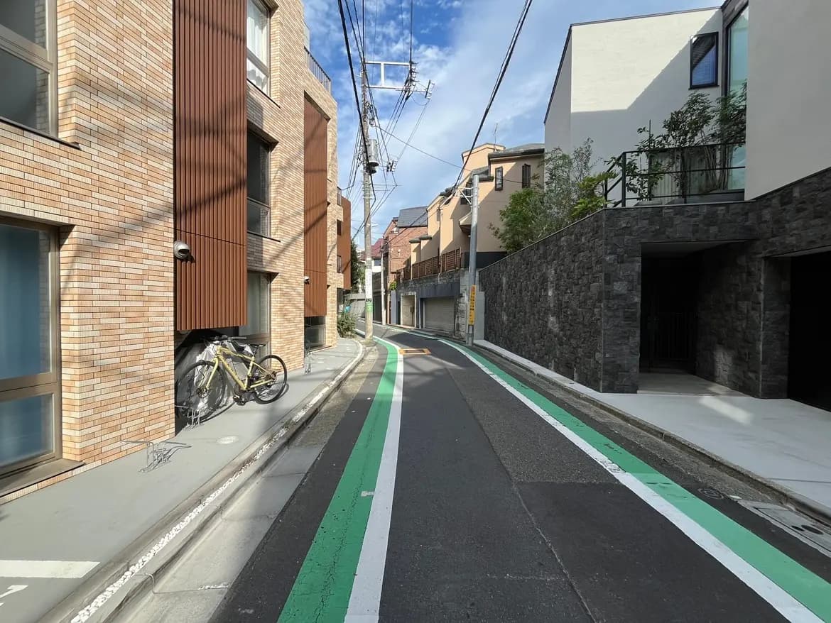 - 都市の住宅街にある自転車が置かれたレンガ造りの建物と、緑のラインが引かれた車道が見える風景