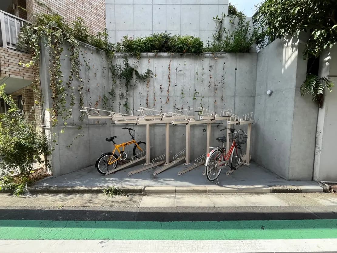 - 自転車が停められたコンクリート製の駐輪場、緑の植物が絡まった壁と自転車ラックが特徴的な風景