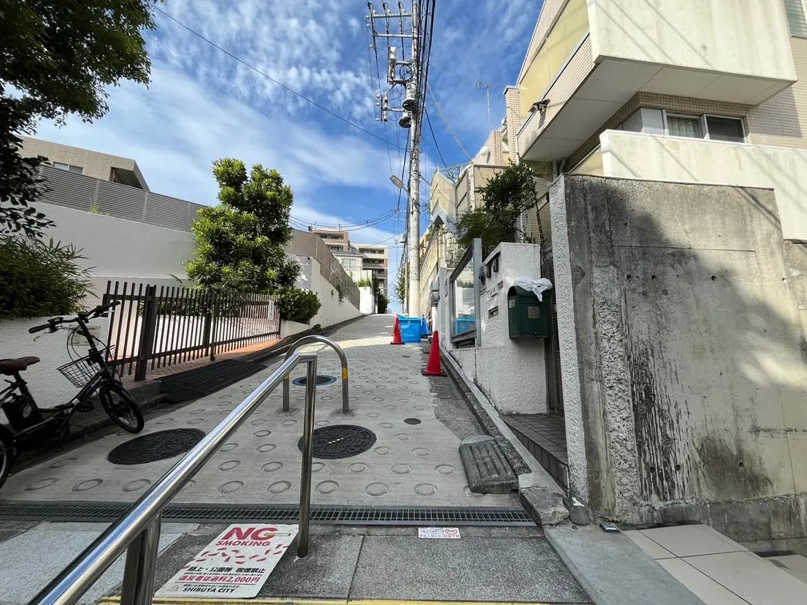 - 坂道を上がる景観、左側に自転車が置かれ、障害物のない手すり付きの歩道が見える住宅街の風景
