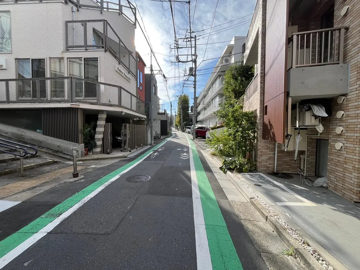 - 緑の自転車レーンがある静かな住宅街の風景、近代的な建物が並び、空には青空が広がる様子