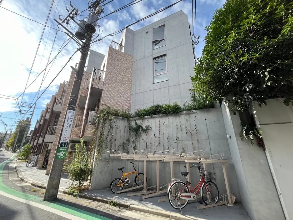 - 近代的なコンクリートとレンガの外観を持つアパート、掃き出し窓、道沿いに自転車置き場と電柱がある風景