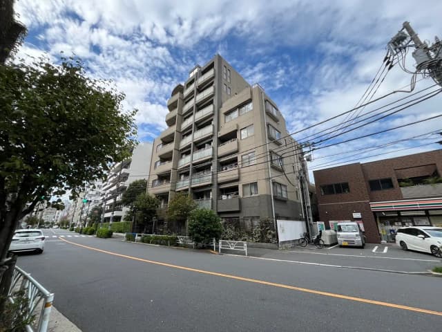 - 近代的なマンションが立ち並ぶ都会の風景、青空と雲が広がる、道路沿いの植栽と車両が見える景色