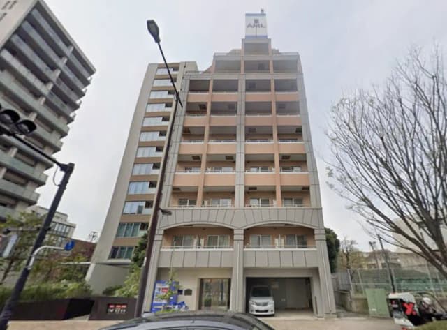 - モダンな外観のマンションビル、周囲に並ぶ高層建築と緑豊かな景観、車道沿いに位置するエントランスが特徴の建物