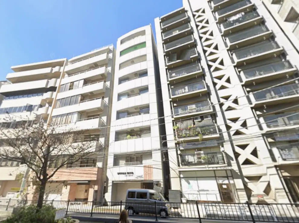 - 都市型マンションの外観、複数のバルコニーと大きな窓、晴れた青空の背景に建つビル群