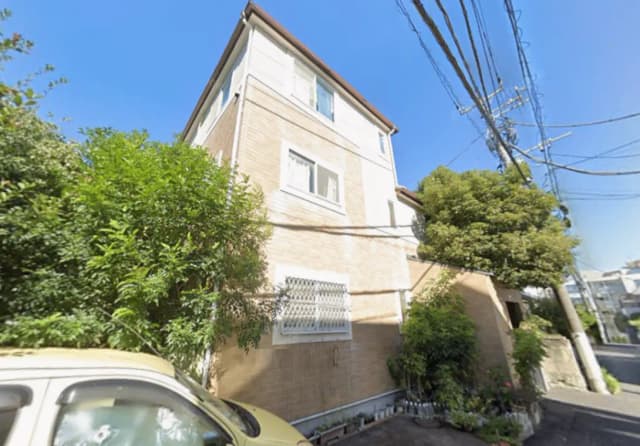 - 自然に囲まれた外観の3階建て住宅、青空と電線が見える通りの風景、緑豊かな植栽が特徴的な住宅地