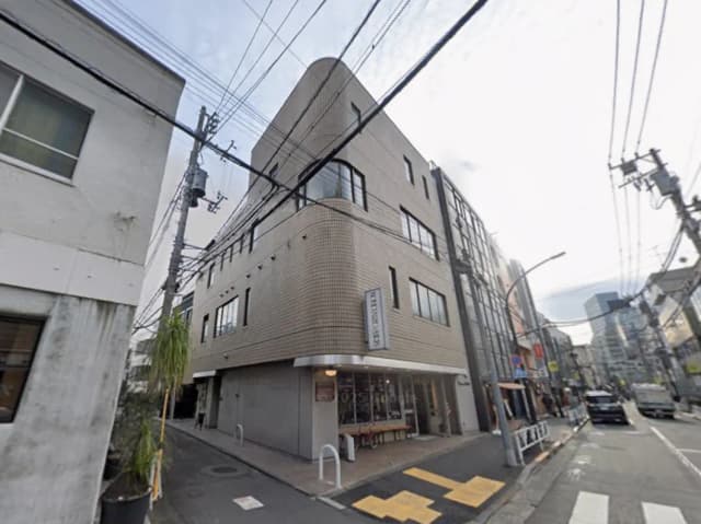 - 角地に建つ現代的な商業ビル、窓が多く明るい外観、周辺の街並みや電柱が見える風景