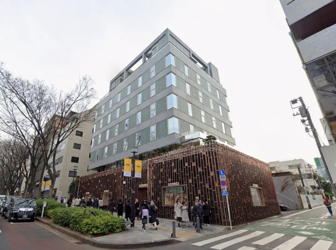 - 現代的なデザインの建物と高級ブランド「エルメス」の店舗、通りには多くの人々が行き交う様子