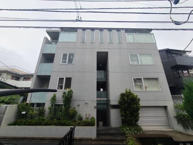 - モダンなコンクリート製のマンション外観、ガラスのバルコニーと緑豊かな植栽が特徴的な住宅ビル