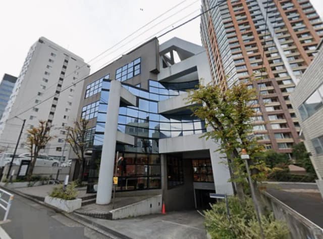 - モダンな建築デザインのビル外観、ガラス面が多く採用されたファサードと円形の柱、周囲に緑がある街並み