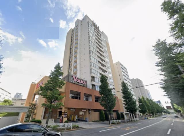 - 高層マンションの外観、下部にレストラン「VOLKS」がある、青空と並木が見える風景