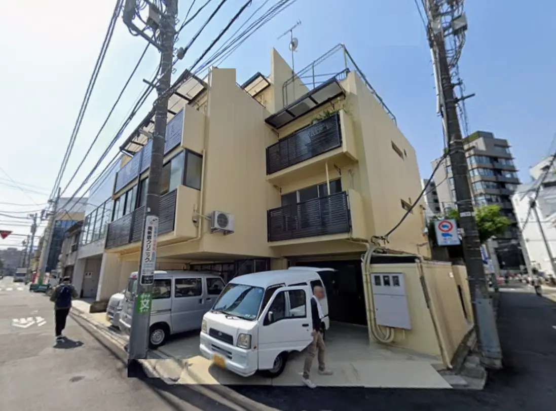 - 近代的なデザインの三階建て住宅、バルコニーと大きな窓が特徴、周囲に電柱と車がある通りの風景