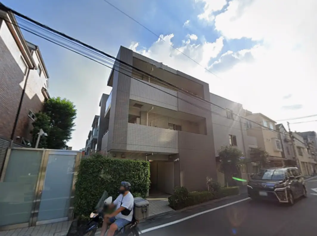 - シンプルでモダンな外観のアパートメントビル、周囲には緑豊かな植栽と自転車が通る通りの風景