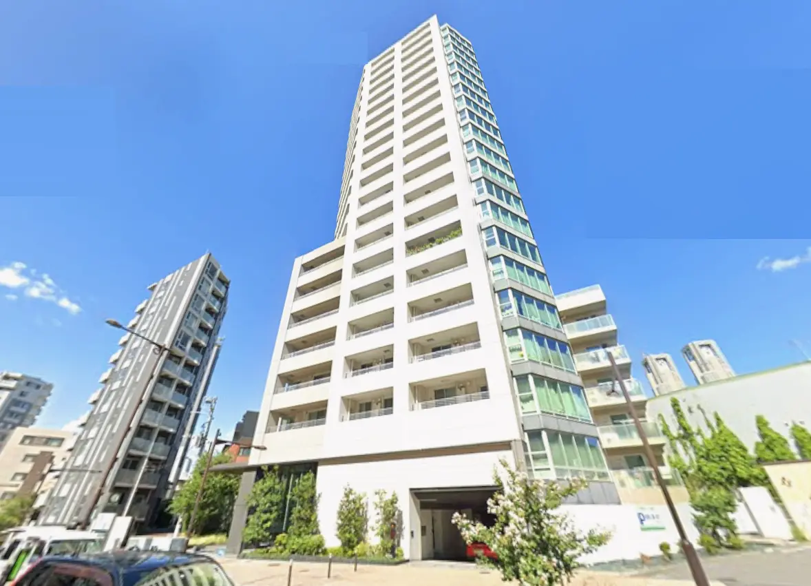 高層マンションの外観、青空を背景にしたモダンなデザインとバルコニー、周囲に立つ他の建物が見える景観