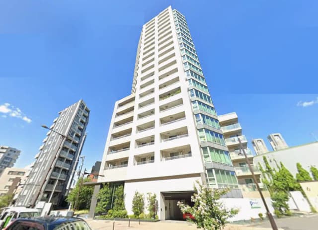 高層マンションの外観、青空を背景にしたモダンなデザインとバルコニー、周囲に立つ他の建物が見える景観