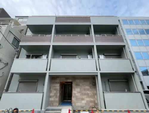 - モダンな外観のアパートメントビル、3階建てのバルコニーと石材のエントランス、周囲の街並みが見える景色