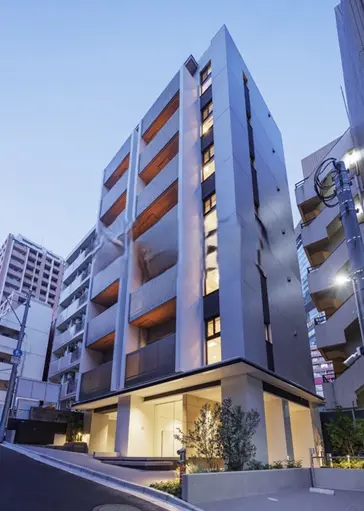 - モダンなデザインの高層マンション、都市の風景に溶け込む外観、夜の照明が際立つエントランス周辺