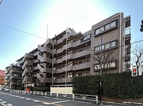 - モダンなデザインの集合住宅、特徴的なバルコニーと緑の生垣に囲まれた外観のビル