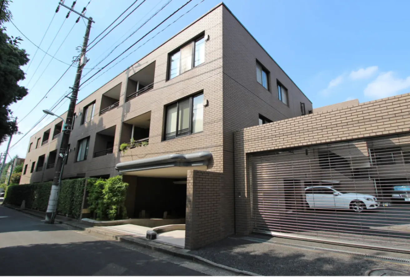 - モダンな外観のアパートメントビル、植栽に囲まれたエントランスとガレージ、青空の下での建物の全体像