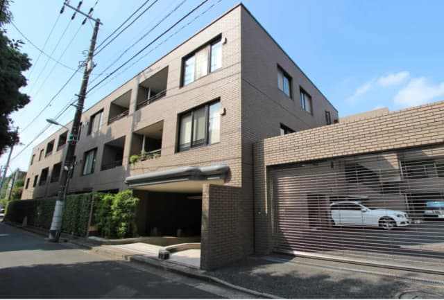 - モダンな外観のアパートメントビル、植栽に囲まれたエントランスとガレージ、青空の下での建物の全体像