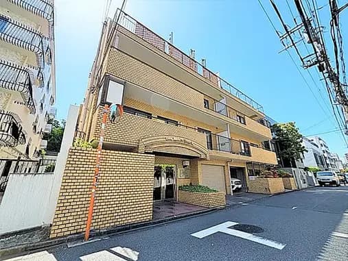 - 明るい日差しの下で撮影されたレンガ造りのアパートメントビル、周囲に緑が見える静かな通りの景観