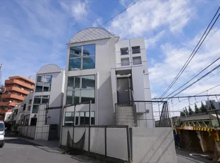 - モダンなデザインの集合住宅、ガラス張りの外装と特徴的な屋根、青空を背景にした外観