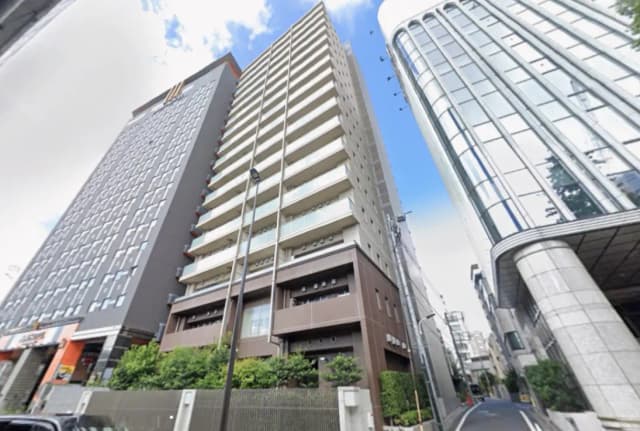 - 都市景観の中に立つモダンな高層マンション、明るい青空と周囲のビル群とのコントラストが印象的な写真