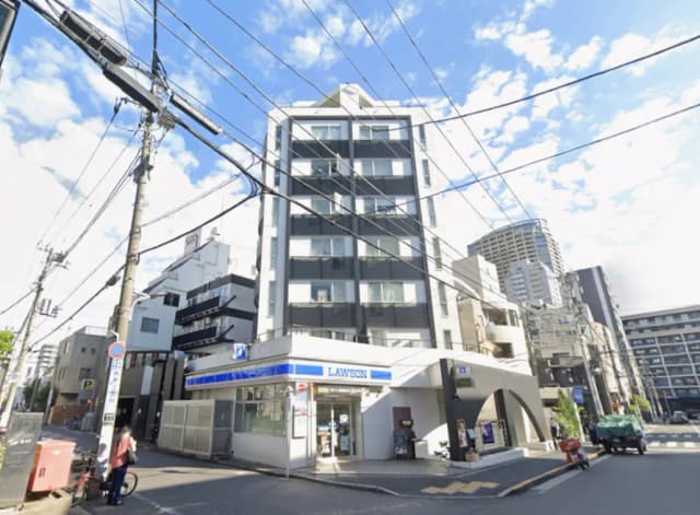 - ローソンの店舗があるビルの外観、周囲には高層ビルと電信柱、青空が広がる都市風景