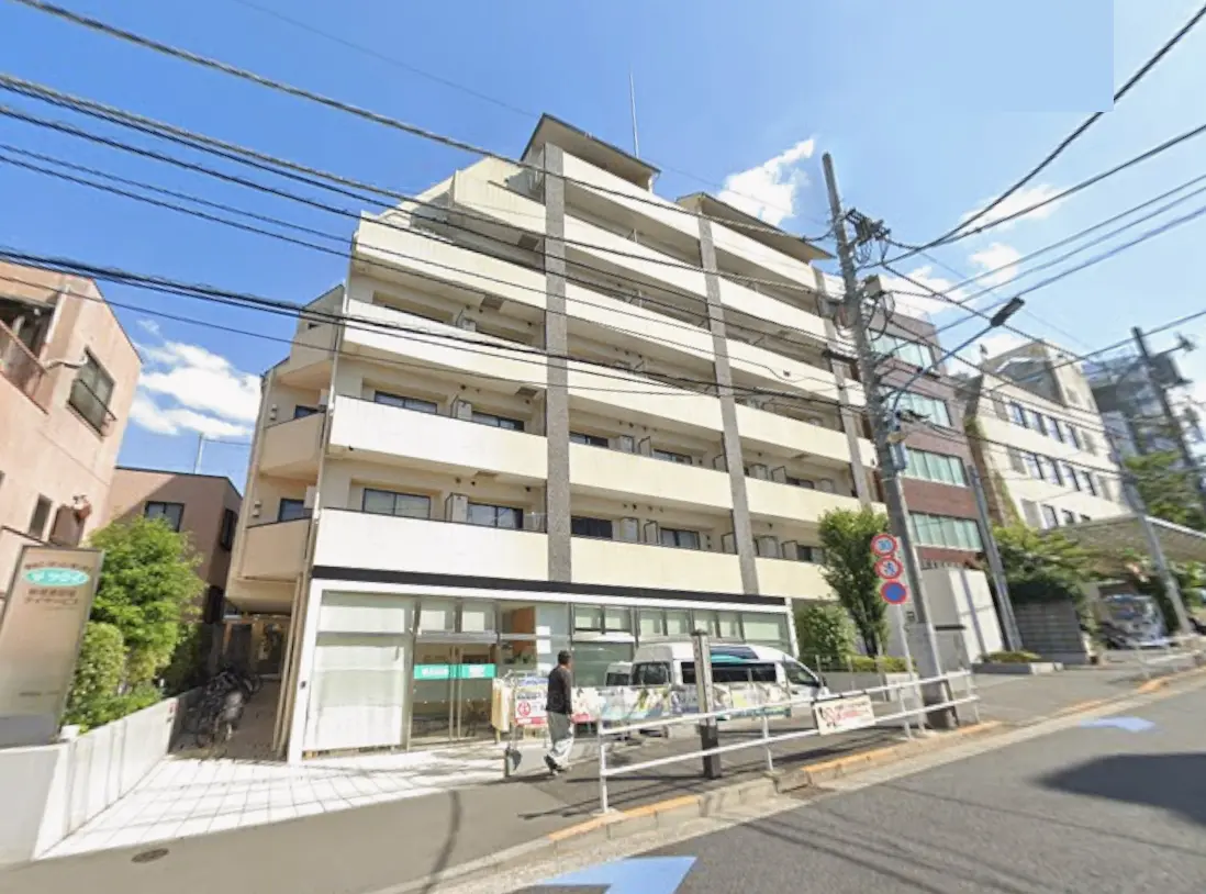 - 明るい青空の下にある4階建てのアパートメントビル、白い外壁と特徴的なタイルデザイン、多くの窓が並ぶ外観