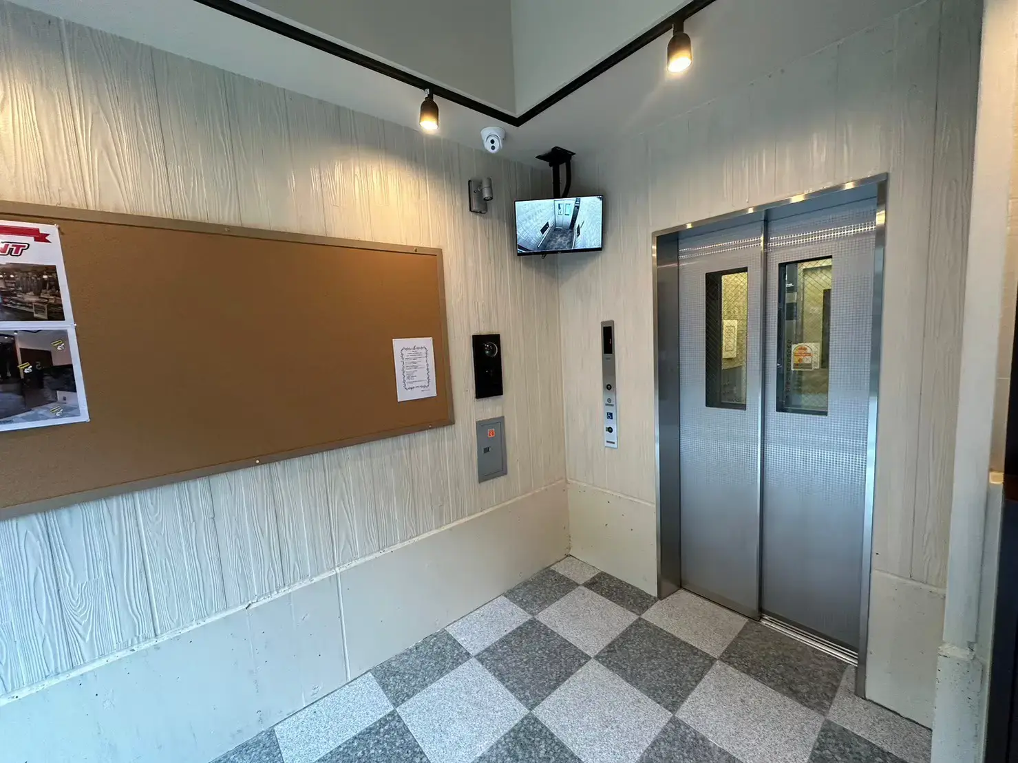木目調の壁面とタイル床が特徴的なエントランスホール、セキュリティモニター付きエレベーター