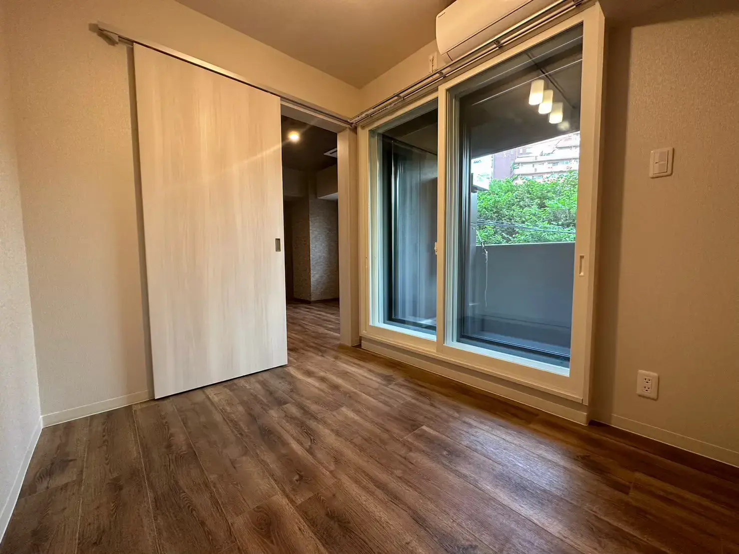 木目調フローリングの広々とした居間、スライディングドアとバルコニー付き