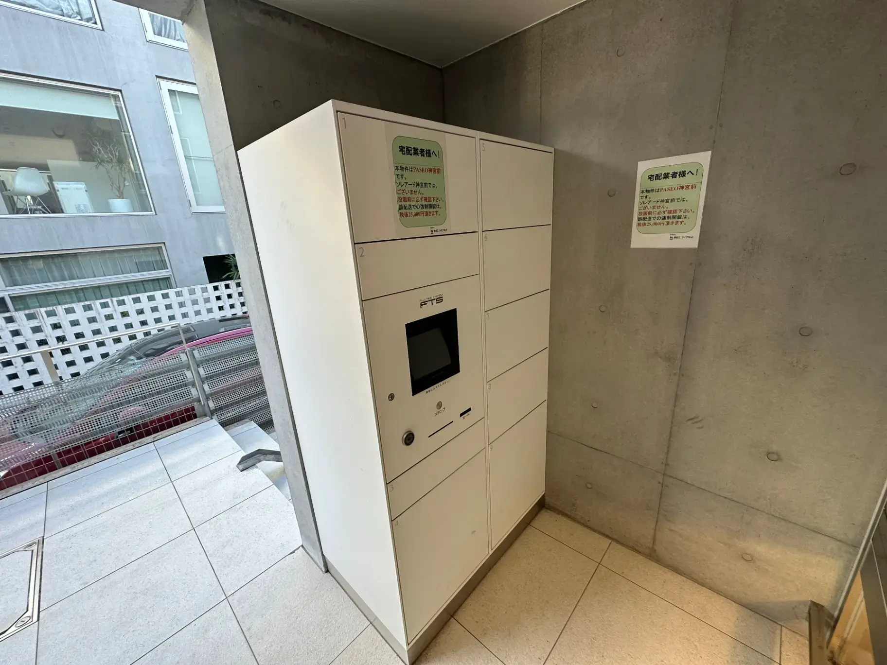 室内に設置された宅配ボックス、コンクリート打ちっぱなしの壁、セキュリティカメラつき、明るい光が差し込む空間