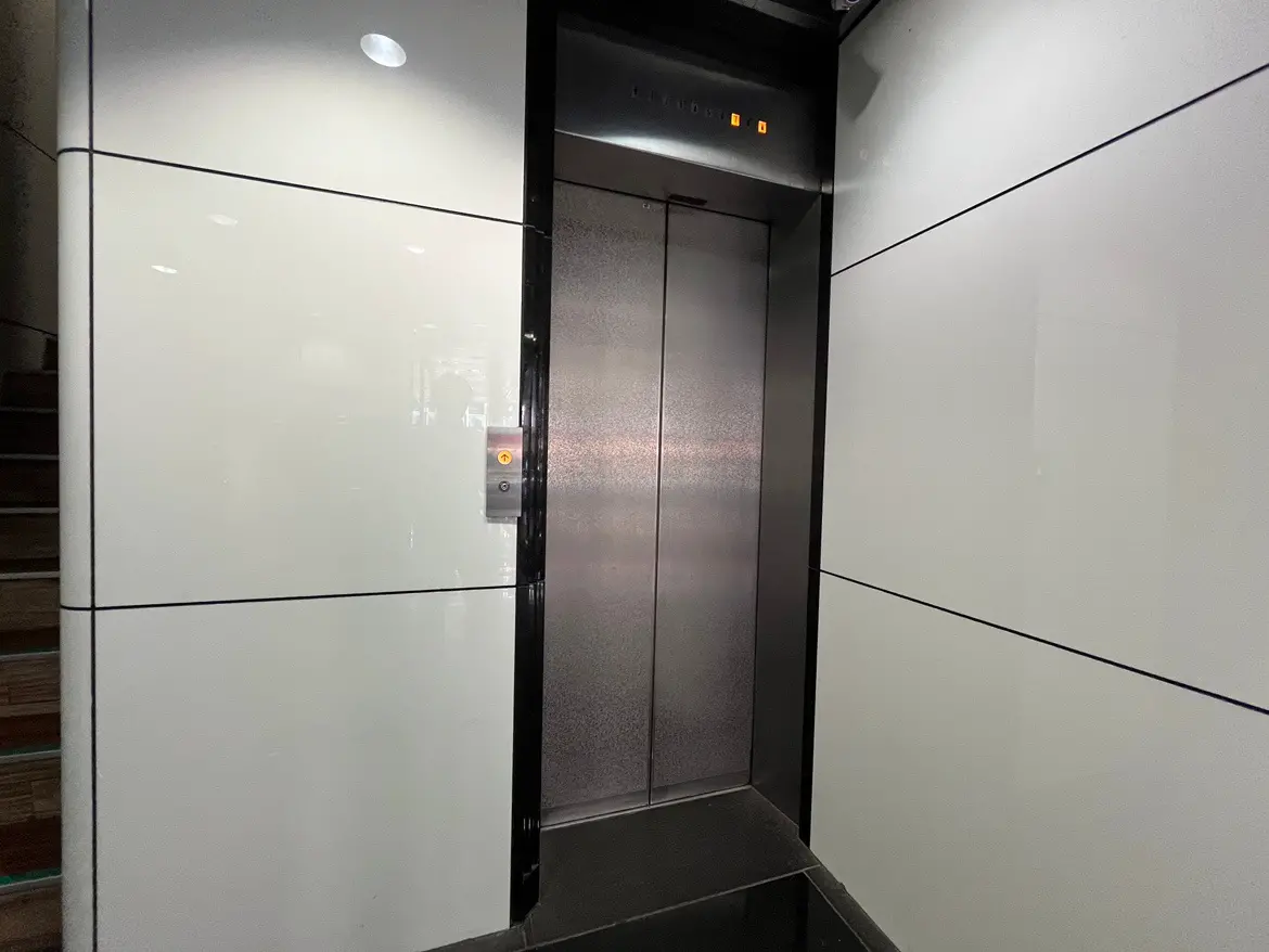 - モダンなデザインのエレベーター入り口、白い壁と黒いアクセント、操作パネルが設置された明るい空間