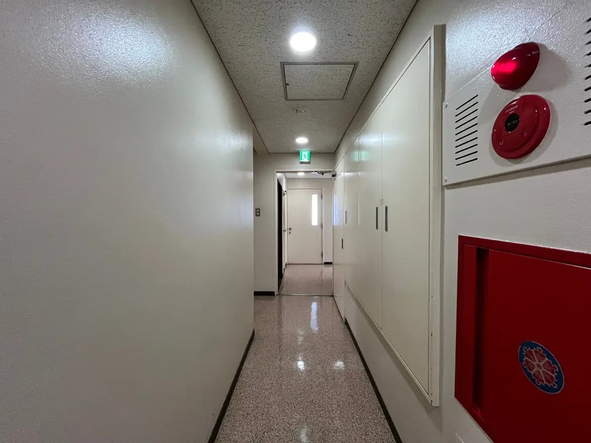 - 明るい照明のある長い廊下、白い壁と防火設備が配置されているシンプルな内部の風景