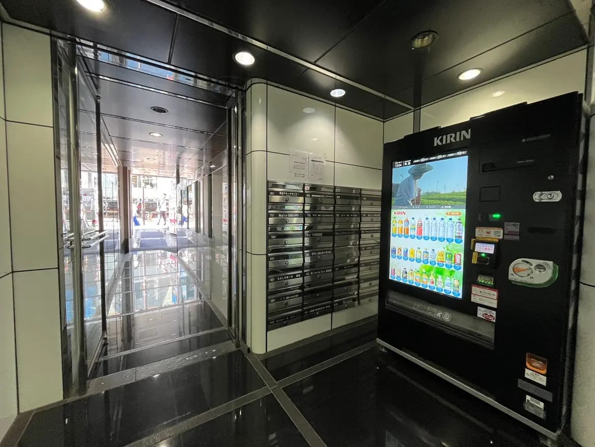 - モダンなエントランスホール、透明なエレベーター、郵便ボックスと自動販売機が並ぶ洗練されたインテリア