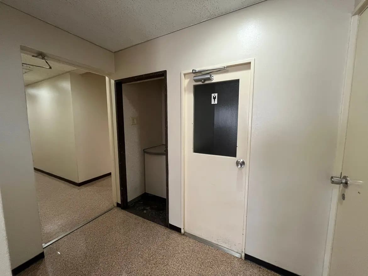 - シンプルなデザインの廊下、左側にトイレのドア、右側に小さな収納スペースがある内部の様子