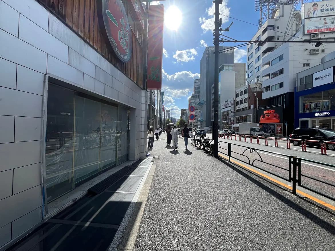 - 明るい日差しが差し込む街並み、歩道を歩く人々と自転車、ビルが立ち並ぶ景観