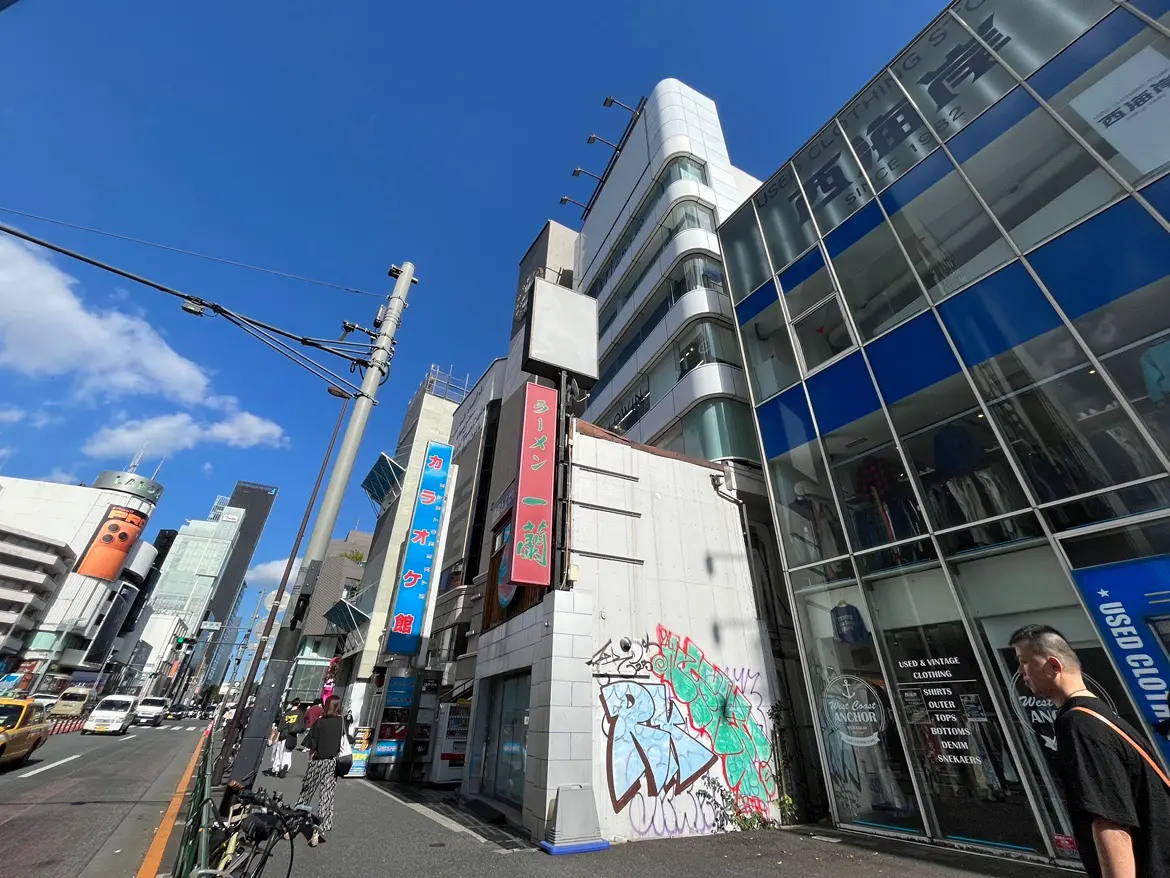 - 明るい青空の下、賑やかな街並みと様々な店舗が並ぶ通り、ガラス張りの建物や路面店が見える風景